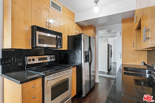 kitchen with appliances with stainless steel finishes, dark wood-type flooring, dark stone countertops, and decorative backsplash