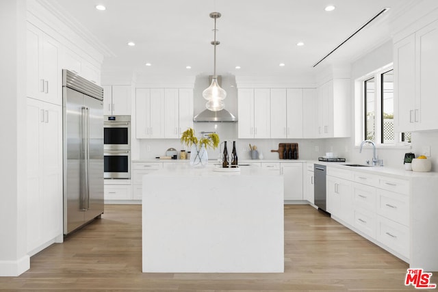 kitchen featuring white cabinetry, hanging light fixtures, stainless steel appliances, a kitchen island, and wall chimney exhaust hood