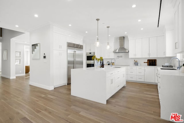 kitchen featuring appliances with stainless steel finishes, white cabinetry, sink, a kitchen island with sink, and wall chimney exhaust hood