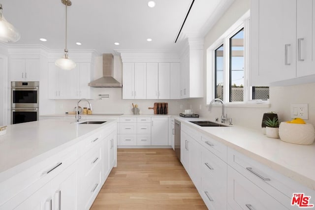 kitchen featuring decorative light fixtures, sink, white cabinets, stainless steel appliances, and wall chimney range hood