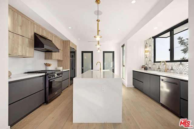 kitchen with a kitchen island with sink, hanging light fixtures, stainless steel appliances, light stone countertops, and light wood-type flooring