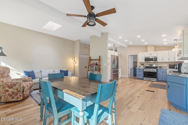 dining room featuring lofted ceiling with skylight, ceiling fan, and light wood-type flooring