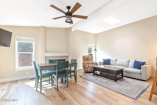 living room with lofted ceiling with beams, a tile fireplace, ceiling fan, and light hardwood / wood-style floors