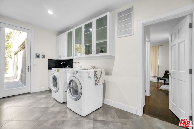 washroom with separate washer and dryer, light tile patterned floors, and cabinets