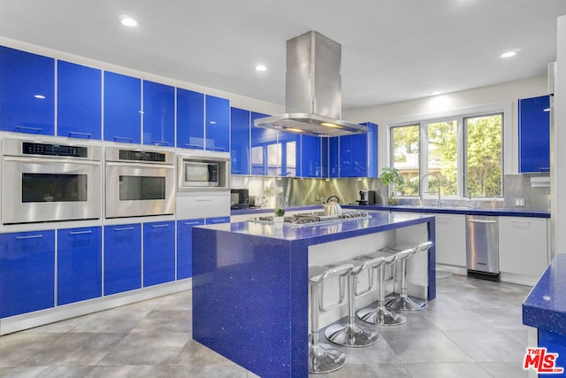 kitchen with sink, appliances with stainless steel finishes, island exhaust hood, a kitchen island, and decorative backsplash