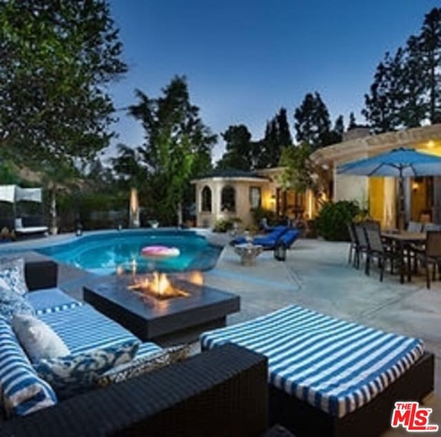 pool at dusk featuring an outbuilding, a patio area, and an outdoor living space with a fire pit