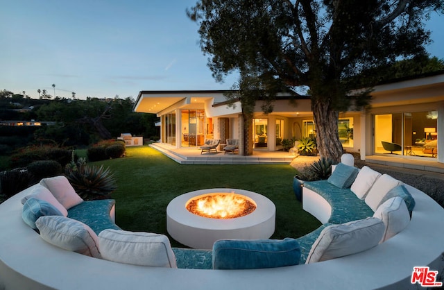 pool at dusk with a lawn, an outdoor living space with a fire pit, and a patio