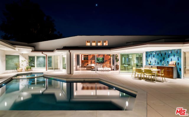 pool at night featuring a patio area