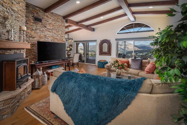 living room with beam ceiling, high vaulted ceiling, a wood stove, and light hardwood / wood-style floors