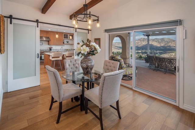 dining space featuring lofted ceiling with beams, a barn door, light hardwood / wood-style floors, and a notable chandelier