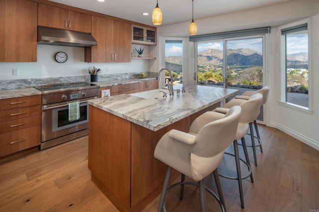 kitchen featuring pendant lighting, sink, a kitchen island with sink, a kitchen breakfast bar, and stainless steel electric stove