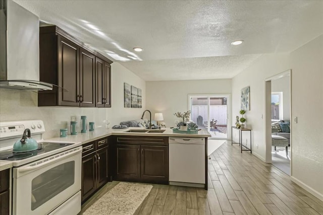 kitchen with sink, light wood-type flooring, kitchen peninsula, white appliances, and wall chimney range hood