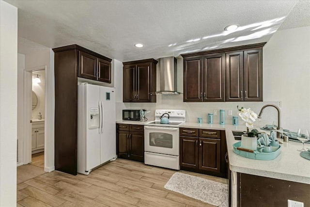 kitchen featuring sink, dark brown cabinets, white appliances, light hardwood / wood-style floors, and wall chimney range hood