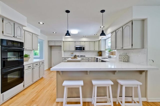 kitchen with black double oven, light hardwood / wood-style floors, a kitchen bar, decorative backsplash, and kitchen peninsula