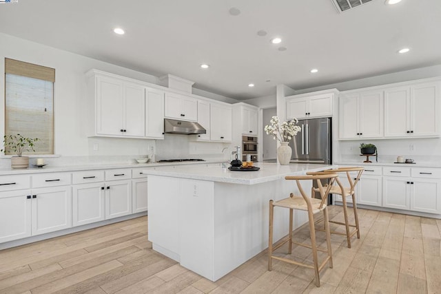 kitchen featuring a breakfast bar area, white cabinets, stainless steel appliances, a center island with sink, and light wood-type flooring