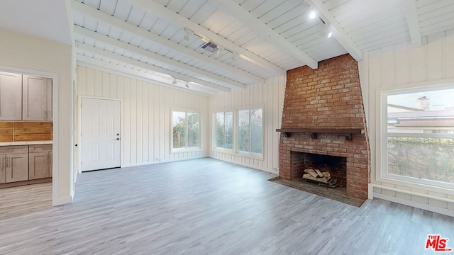 unfurnished living room featuring beamed ceiling, plenty of natural light, light hardwood / wood-style floors, and a brick fireplace