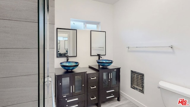 bathroom with heating unit, vanity, wood-type flooring, and toilet