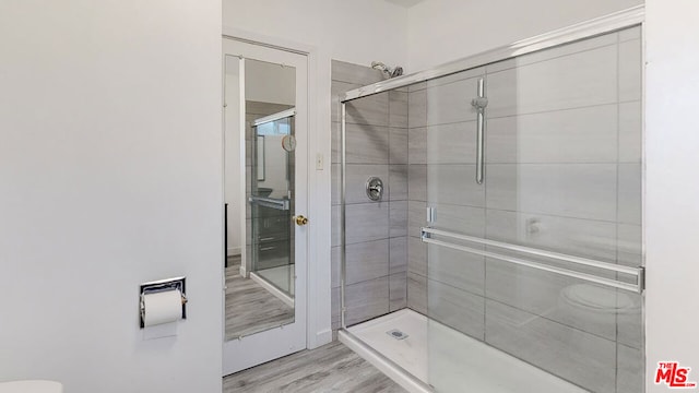 bathroom with hardwood / wood-style floors, a shower with shower door, and toilet