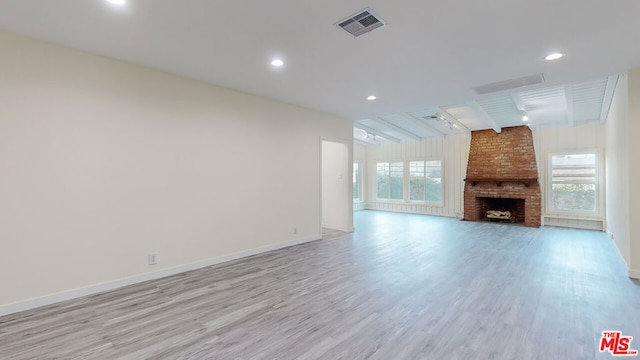 unfurnished living room with plenty of natural light, a brick fireplace, light hardwood / wood-style flooring, and vaulted ceiling with beams