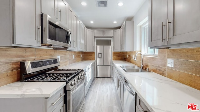 kitchen featuring sink, gray cabinetry, stainless steel appliances, light stone countertops, and decorative backsplash