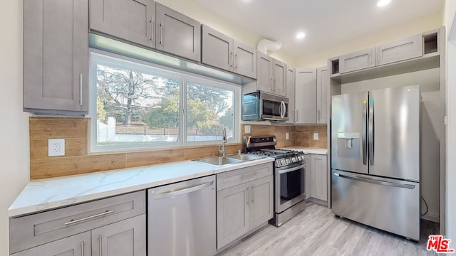 kitchen with gray cabinets, sink, backsplash, stainless steel appliances, and light stone countertops