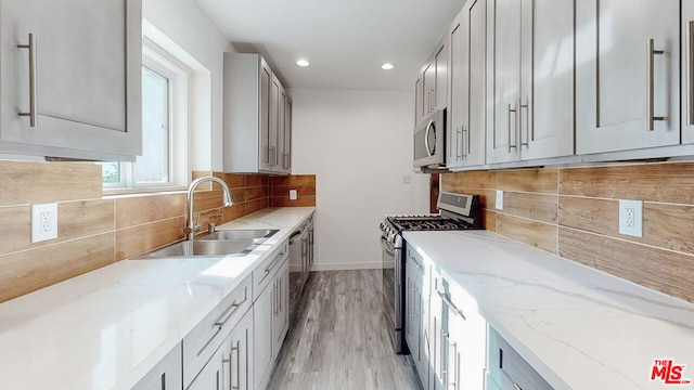 kitchen featuring sink, gray cabinetry, light stone counters, tasteful backsplash, and stainless steel appliances