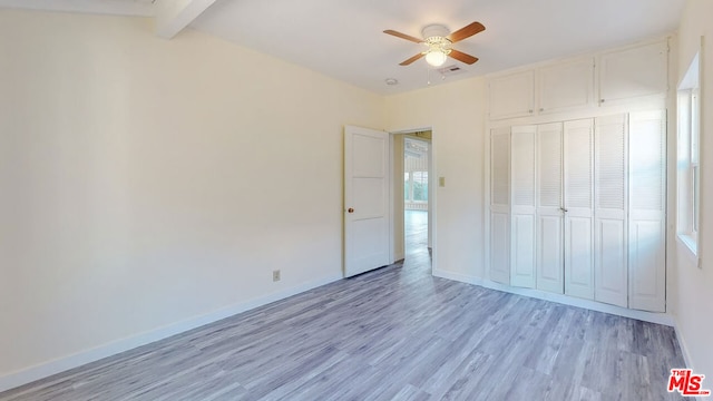 unfurnished bedroom with ceiling fan, light wood-type flooring, beam ceiling, and a closet