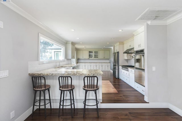 kitchen featuring stainless steel appliances, white cabinets, a kitchen bar, decorative backsplash, and kitchen peninsula