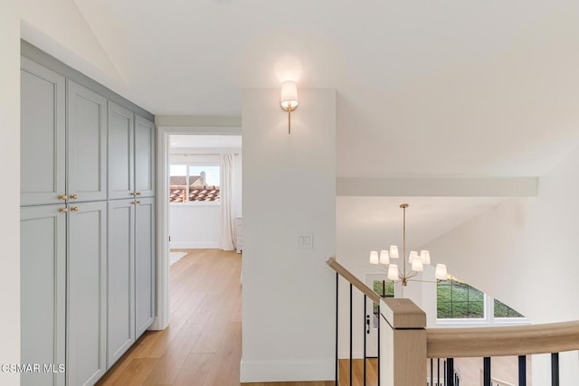 corridor featuring lofted ceiling, light hardwood / wood-style floors, and a chandelier