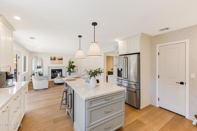 kitchen with a kitchen island, white cabinets, a kitchen breakfast bar, hanging light fixtures, and high end fridge