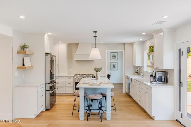 kitchen featuring high end appliances, premium range hood, hanging light fixtures, and white cabinets