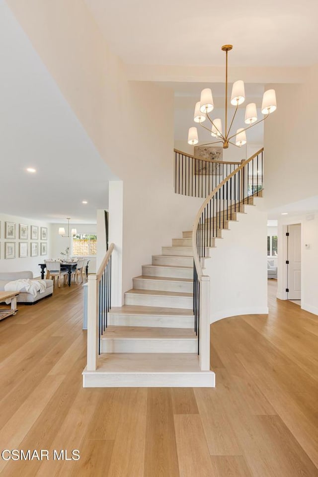 stairway featuring an inviting chandelier, a towering ceiling, and wood-type flooring