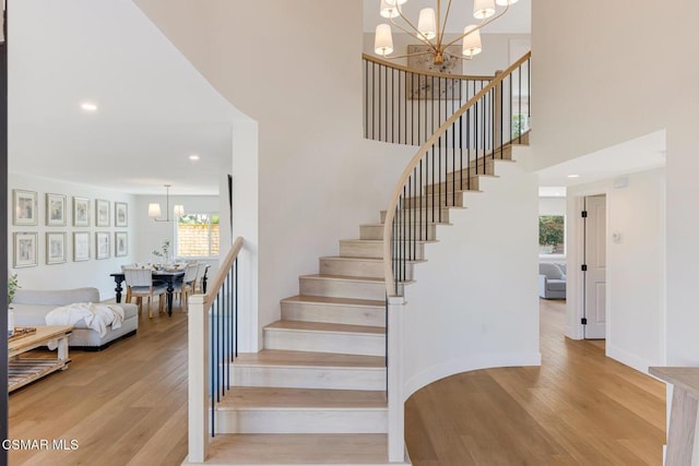 stairs with a towering ceiling, a chandelier, and hardwood / wood-style floors