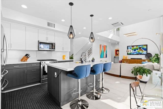 kitchen with a breakfast bar, decorative light fixtures, white cabinetry, a kitchen island with sink, and stainless steel appliances