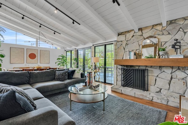 living room with track lighting, wood-type flooring, a stone fireplace, and vaulted ceiling with beams