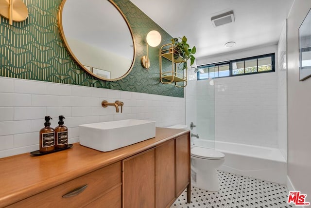 full bathroom featuring tile patterned floors, toilet, tiled shower / bath, tile walls, and vanity