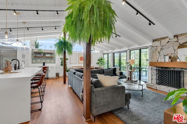 living room featuring rail lighting, sink, vaulted ceiling with beams, a fireplace, and hardwood / wood-style floors