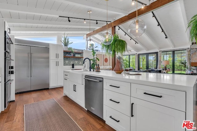 kitchen featuring hardwood / wood-style flooring, appliances with stainless steel finishes, vaulted ceiling with beams, and white cabinets