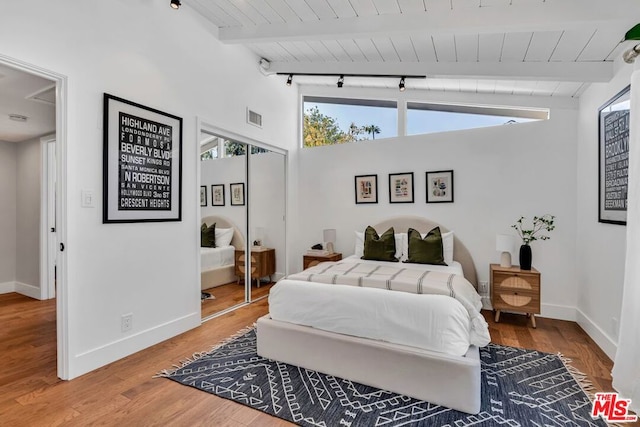 bedroom featuring lofted ceiling with beams, rail lighting, wood-type flooring, and wood ceiling