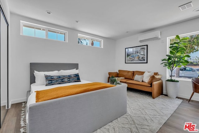 bedroom featuring a wall mounted AC and light hardwood / wood-style floors