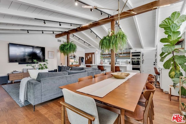 dining room featuring rail lighting, light wood-type flooring, and vaulted ceiling with beams