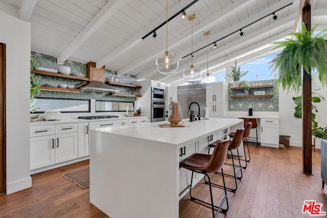 kitchen featuring a breakfast bar, pendant lighting, stainless steel appliances, a kitchen island with sink, and white cabinets