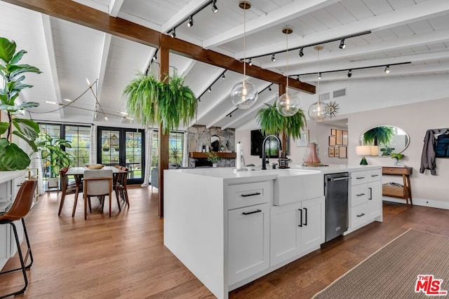 kitchen with hardwood / wood-style floors, pendant lighting, white cabinetry, vaulted ceiling with beams, and a kitchen island with sink