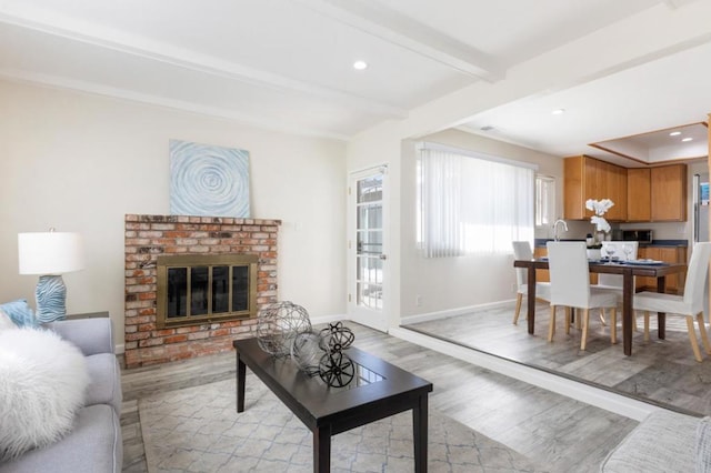 living room with a brick fireplace, beam ceiling, and light hardwood / wood-style floors