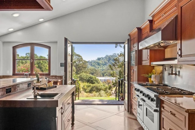 kitchen with double oven range, vaulted ceiling, sink, and wall chimney exhaust hood