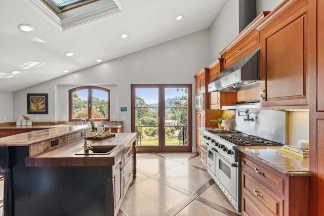 kitchen featuring wall chimney exhaust hood, lofted ceiling, sink, an island with sink, and stainless steel appliances