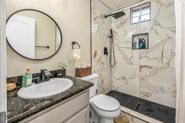 bathroom featuring a tile shower, vanity, and toilet