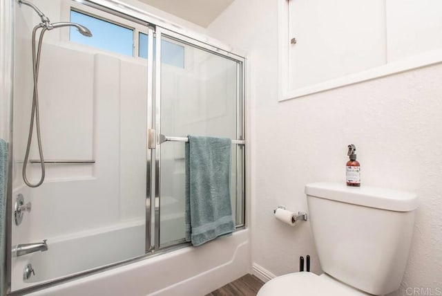 bathroom with combined bath / shower with glass door, hardwood / wood-style floors, and toilet