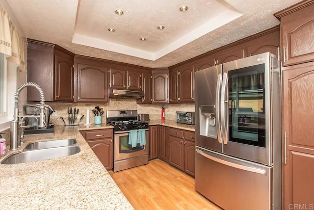 kitchen featuring sink, light hardwood / wood-style flooring, stainless steel appliances, a textured ceiling, and a raised ceiling