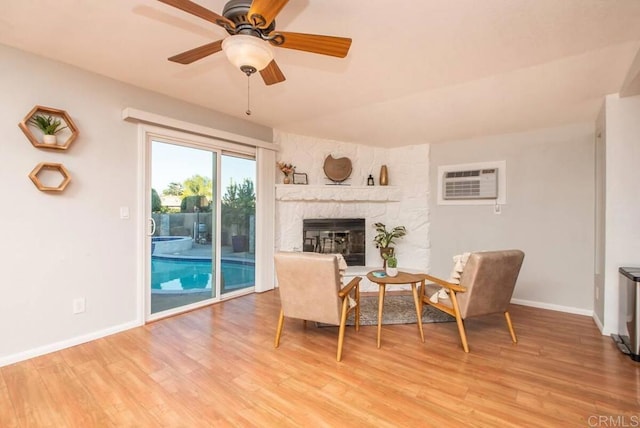 living area featuring ceiling fan, a stone fireplace, a wall mounted AC, and light hardwood / wood-style flooring